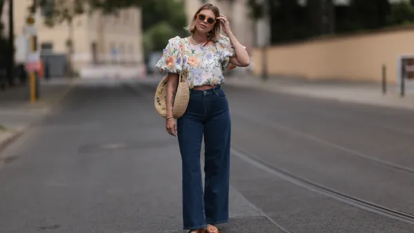 Aline Kaplan wearing Baum & Pferdgarten wide leg blue denim pants, & other stories white flower pattern cropped blouse and orange summer heels and Mango orange black shades on June 06, 2023 in Berlin, Germany.