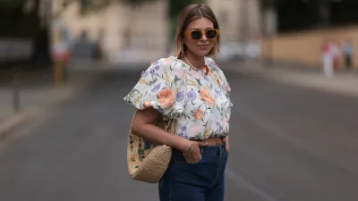 Aline Kaplan wearing Baum & Pferdgarten wide leg blue denim pants, & other stories white flower pattern cropped blouse and orange summer heels and Mango orange black shades on June 06, 2023 in Berlin, Germany.