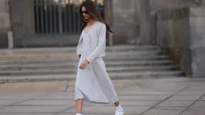 Jill Asemota seen wearing black vintage sunglasses, Dorothee Schumacher grey wool knit long dress, matching Dorothee Schumacher grey wool knit cardigan jacket, white cotton socks, Adidas white leather Samba sneakers, on November 04, 2023 in Berlin, Germany.