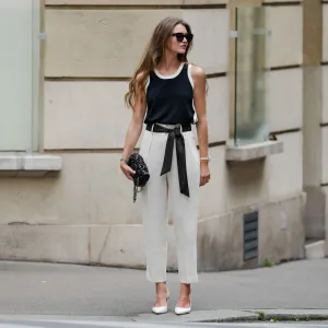 Segolene Hyppolite wears sunglasses, red lipstick / make-up, a dark navy blue / black and white tank top from Tara Jarmon, a black Chanel bag with floral textures / details, a Chanel watch, a black and white polka dots printed knot / scarf belt, a white floral shaped bracelet, white cropped pants from Tara Jarmon, white pumps / pointed shoes from Jonak, during a street style fashion photo session, on May 12, 2024 in Paris, France.