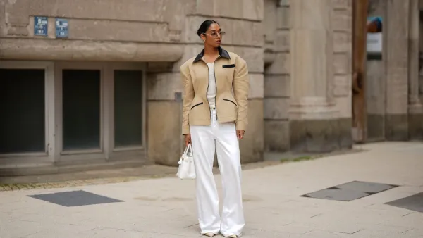 HAMBURG, GERMANY - JUNE 4: Cherifa Akili is seen wearing dark brown hair in a sleek bun, a beige hourglass canvas work jacket with strong padded shoulders and black contrast leather collar and pocket details from Source Unknown, a white wide leg baggy jeans from Closed, a new white Swift leather Birkin 25 bag with golden hardware from Hermès, a pair of off white Kiss stiletto pumps with pointed toe from Saint Laurent, an ecru lightweight ribbed t-shirt with round neckline from Closed, pale gold TF3104D sunglasses with rimless metal frame and gradient lenses, small silver hoop earrings with structure, a yellow gold Toi et Moi ring stacked with diamonds from ÉLOUISE, a silver engagement ring with green gemstone on June 4, 2025 in Hamburg, Germany. (Footage by Moritz Scholz/Getty Images)