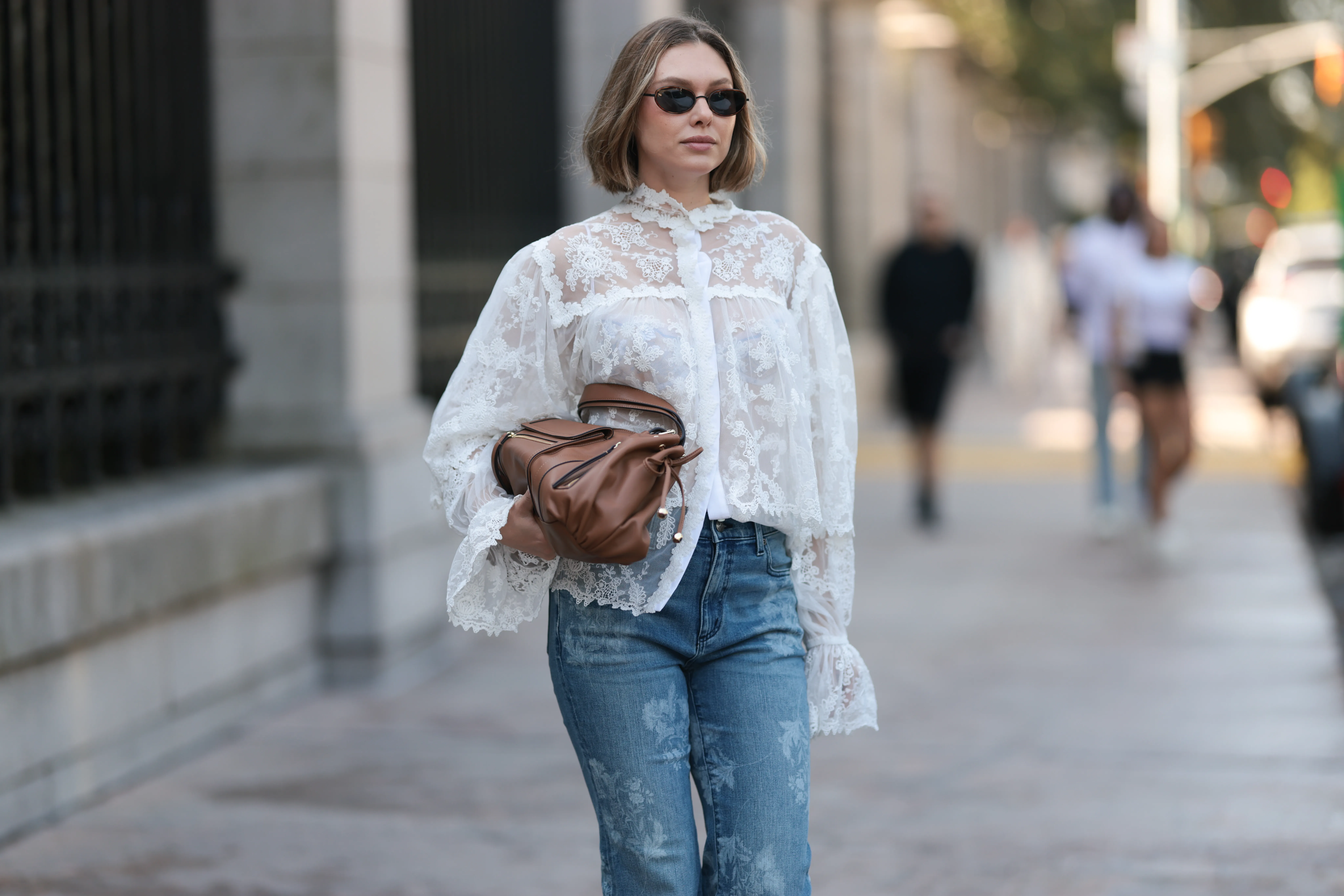 NEW YORK, NEW YORK - SEPTEMBER 14: Kate Smolianinova seen wearing Vehla Eyewear slim rectangular sunglasses in a dark brown. Her hair styled in a sleek chin-length bob with a soft middle part. A Kobi Halperin sheer white lace blouse with floral embroidery, high ruffled collar, voluminous sleeves and scalloped edges, paired with Kobi Halperin blue high-waist flared jeans featuring tonal floral jacquard detailing and a Gerard Darel soft brown leather handbag with gathered pleats and rounded handles, outside the Ulla Johnson show, during New York Fashion Week, on September 14, 2025 in New York City. (Photo by Jeremy Moeller/Getty Images)