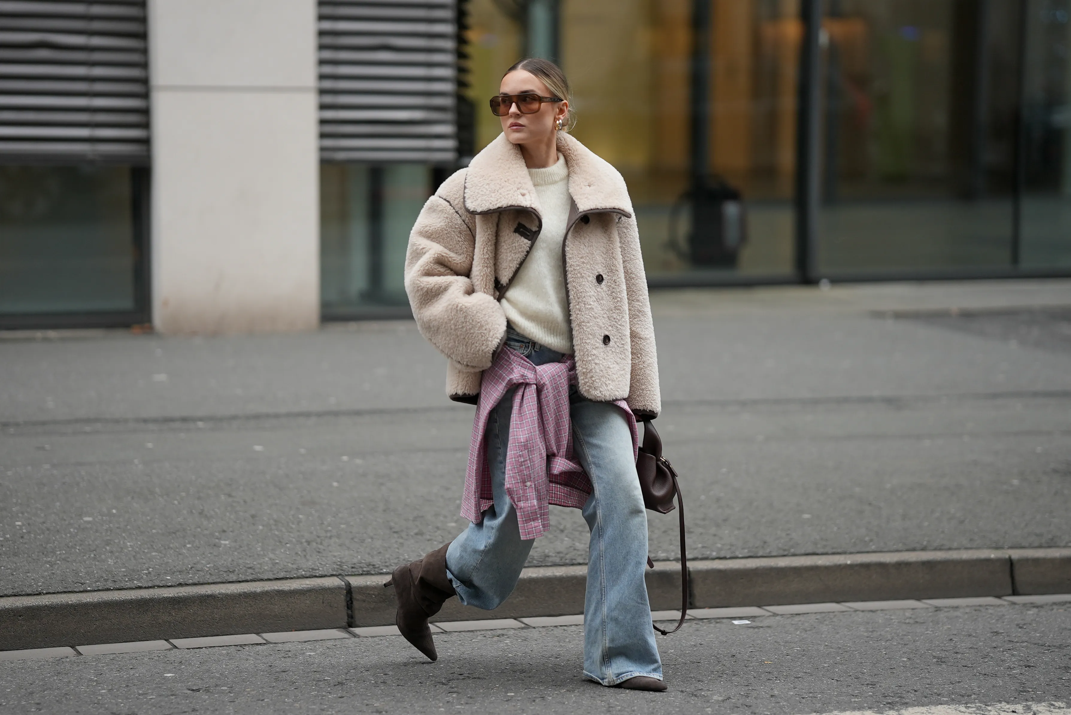 DUESSELDORF, GERMANY - DECEMBER 3: Romina Meier is seen wearing a cropped beige teddy shearling jacket with an oversized collar and contrasting dark brown leather seam detailing from Arket; an off-white fluffy knit pullover from Surprise Paris; a pink and white checkered button-up Borrowed flannel shirt from Our Legacy styled casually tied around her hips; light blue straight-leg jeans with a relaxed fit from Levi’s; dark brown suede pointed-toe heeled boots from Mango; a small sculptural Numéro Neuf leather bag in deep brown sandalwood from Polène; big rectangular shaped brown sunglasses from Vehla; mid-sized hoop earrings from high by honey; her blonde hair is styled in a sleek low bun on December 3, 2025 in Duesseldorf, Germany. (Photo by Moritz Scholz/Getty Images)