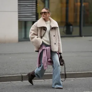 DUESSELDORF, GERMANY - DECEMBER 3: Romina Meier is seen wearing a cropped beige teddy shearling jacket with an oversized collar and contrasting dark brown leather seam detailing from Arket; an off-white fluffy knit pullover from Surprise Paris; a pink and white checkered button-up Borrowed flannel shirt from Our Legacy styled casually tied around her hips; light blue straight-leg jeans with a relaxed fit from Levi’s; dark brown suede pointed-toe heeled boots from Mango; a small sculptural Numéro Neuf leather bag in deep brown sandalwood from Polène; big rectangular shaped brown sunglasses from Vehla; mid-sized hoop earrings from high by honey; her blonde hair is styled in a sleek low bun on December 3, 2025 in Duesseldorf, Germany. (Photo by Moritz Scholz/Getty Images)