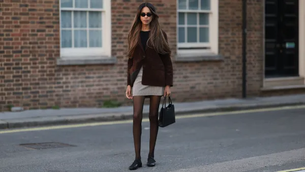 LONDON, ENGLAND - SEPTEMBER 19: Jill Asemota seen wearing a sleek Miu Miu cat-eye sunglasses in glossy black, a chocolate brown suede leather blazer by Zara, cut in a relaxed silhouette with slightly oversized sleeves and flap pockets at the sides, sleek black fitted Wolford top in a minimalist design, Burberry Vintage mini skirt in a beige-and-brown check houndstooth pattern, tailored to a straight cut, sheer black tights, classic black Chanel Mary Jane flats, crafted in smooth leather and a structured black vintage handbag, boxy in shape with short handles and metallic hardware details. Her brown hair is styled in a long, straight blowout with subtle caramel highlights, parted naturally and falling over her shoulders, during London Fashion Week on September 19, 2025 in London, England. (Photo by Jeremy Moeller/Getty Images)