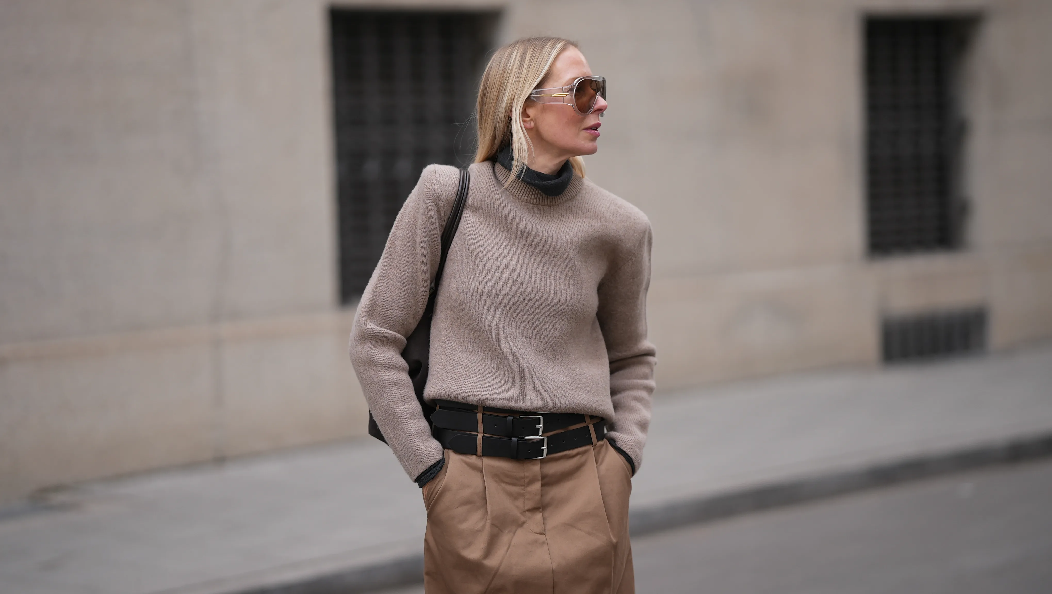 MUNICH, GERMANY - JANUARY 22: Mirja Klein is seen wearing a dark grey turtleneck sweater with slim fit from The Frankie Shop; a beige sweater with padded shoulders, crew neck and long sleeves layered over from COS; a light brown midi skirt with pleated front pockets, A-line silhouette and three black layered leather belts with silver buckles from MeiMeij; oversized shield sunglasses with transparent acetate frame and brown tinted lenses from Bottega Veneta; a dark chocolate brown suede leather shoulder bag with smooth leather top handles called "The Midi Stockholm&sbquo;&Auml;&uacute; from DeMellier; her blonde hair is worn straight and open, parted in the middle on January 22, 2026 in Munich, Germany. (Photo by Moritz Scholz/Getty Images)