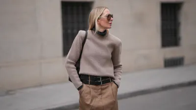 MUNICH, GERMANY - JANUARY 22: Mirja Klein is seen wearing a dark grey turtleneck sweater with slim fit from The Frankie Shop; a beige sweater with padded shoulders, crew neck and long sleeves layered over from COS; a light brown midi skirt with pleated front pockets, A-line silhouette and three black layered leather belts with silver buckles from MeiMeij; oversized shield sunglasses with transparent acetate frame and brown tinted lenses from Bottega Veneta; a dark chocolate brown suede leather shoulder bag with smooth leather top handles called "The Midi Stockholm“ from DeMellier; her blonde hair is worn straight and open, parted in the middle on January 22, 2026 in Munich, Germany. (Photo by Moritz Scholz/Getty Images)