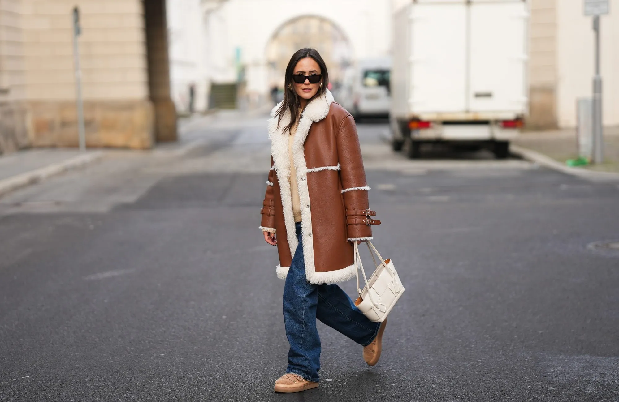 BERLIN, GERMANY - NOVEMBER 25: Laura Noltemeyer is seen wearing a shearling lining coat in a rich cognac tone with an oversized straight silhouette, wide lapels and buckle-strap cuff detailing on the sleeves from Max&Co; layered underneath is a soft beige wool-blend knit sweater with a ribbed crew neckline and ribbed trims from Sézane; dark-blue straight-leg denim trousers with a classic fit from By Aylin Koenig; beige suede winter boots with a rounded toe, exposed stitching and shearling lining from Inuikii; a white structured leather top-handle bag in an intrecciato weave and trapeze silhouette called “Intrecciato Tote” from Bottega Veneta; chunky sculptural gold earrings from Zara; black angular acetate sunglasses with a thick frame and dark lenses from Saint Laurent; her dark-brown hair is worn straight with a center part on November 25, 2025 in Berlin, Germany. (Photo by Moritz Scholz/Getty Images)