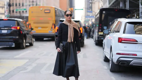 NEW YORK, NEW YORK - FEBRUARY 14: Geraldine Boublil wears a bun, black rectangular sunglasses, earrings, a black leather nailed / studded clutch bag, a beige knit sweater, a black textured jacket, a black leather midi skirt, black sheer tights, black pointed-toe flat shoes with a large bow toe cap, outside Altuzarra, during New York Fashion Week, on February 14, 2026 in New York City (Photo by Edward Berthelot/Getty Images)