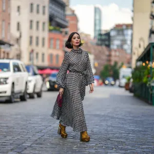 NEW YORK, NEW YORK - SEPTEMBER 12: Heart Evangelista wears golden earrings, a houndstooth pattern printed midi pleated dress, a burgundy leather bag from Carolina Herrera, golden floral print platform boots, outside Carolina Herrera, during New York Fashion Week, on September 12, 2023 in New York City. (Photo by Edward Berthelot/Getty Images)