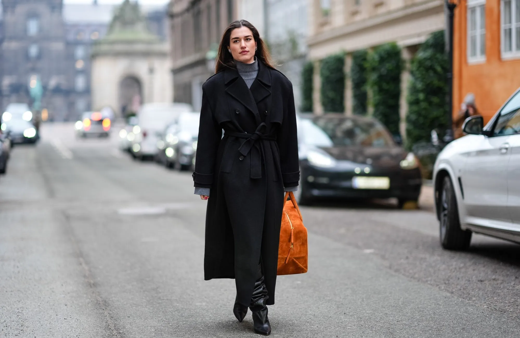 COPENHAGEN, DENMARK - JANUARY 30: A guest wears a gray turtleneck pullover, a black long winter coat, an orange large bag, high heels black leather boots , outside Lovechild 1979, during the Copenhagen Fashion Week AW24 on January 30, 2024 in Copenhagen, Denmark. (Photo by Edward Berthelot/Getty Images)