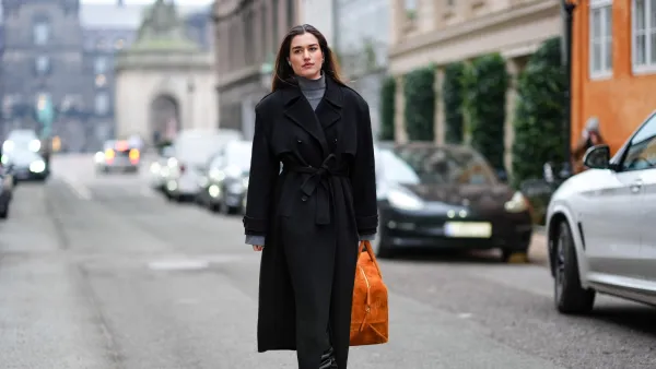COPENHAGEN, DENMARK - JANUARY 30: A guest wears a gray turtleneck pullover, a black long winter coat, an orange large bag, high heels black leather boots , outside Lovechild 1979, during the Copenhagen Fashion Week AW24 on January 30, 2024 in Copenhagen, Denmark. (Photo by Edward Berthelot/Getty Images)