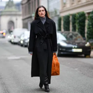 COPENHAGEN, DENMARK - JANUARY 30: A guest wears a gray turtleneck pullover, a black long winter coat, an orange large bag, high heels black leather boots , outside Lovechild 1979, during the Copenhagen Fashion Week AW24 on January 30, 2024 in Copenhagen, Denmark. (Photo by Edward Berthelot/Getty Images)