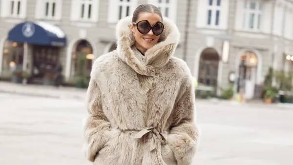 COPENHAGEN, DENMARK - JANUARY 29: Nina Sandbech wears a beige plush faux-fur belted jacket with a high funnel neck, matching beige sheer skirt with fur-trim hems, black glossy knee-high patent leather boots, oversized round black Prada sunglasses during Copenhagen Fashion Week AW26, is seen wearing on January 29, 2026 in Copenhagen, Denmark. (Photo by Raimonda Kulikauskiene/WireImage)