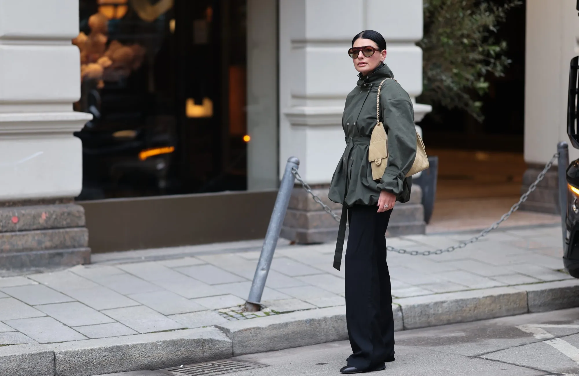 MUNICH, GERMANY - FEBRUARY 1: Sofiya Bogopolska Balci is seen wearing a calligraphy green jacket with a hip belt and buckles on the arms and balloon hems with silver buttons; dark grey wool jumper; straight-cut black fabric trousers from COS; black leather boots with rectangular toes from Ayede; dark brown aviator sunglasses from Prada, silver stud earrings from Cartier; gold and silver rings from Cartier; a silver Rolex; a pastel yellow Chanel 25 bag in caviar leather; her black hair is styled in sleek bun on February 1, 2026 in Munich, Germany. (Photo by Moritz Scholz/Getty Images)