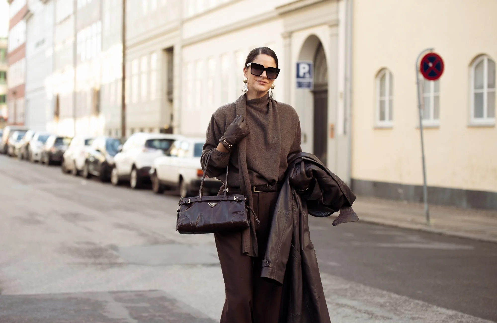 COPENHAGEN, DENMARK - DECEMBER 03: Gili Biegun wears brown tailored trousers, Brown knit with scarf by Massimo Dutti, Celine sunglasses, oversized long Brown leather coat by Herskind, Prada Brown bag, Strathberry Brown leather gloves on December 03, 2024 in Copenhagen, Denmark. (Photo by Raimonda Kulikauskiene/Getty Images)