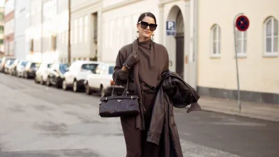 COPENHAGEN, DENMARK - DECEMBER 03: Gili Biegun wears brown tailored trousers, Brown knit with scarf by Massimo Dutti, Celine sunglasses, oversized long Brown leather coat by Herskind, Prada Brown bag, Strathberry Brown leather gloves on December 03, 2024 in Copenhagen, Denmark. (Photo by Raimonda Kulikauskiene/Getty Images)