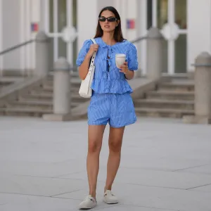 MUNICH, GERMANY - JUNE 15: Anna Winter is seen wearing a blue white striped shorts with drawstring detail from Rita Montezuma x NA-KD; a matching blue white striped blouse with tie and bow details in the front and puff sleeves from Rita Montezuma x NA-KD; a pair of off-white suede Boston slippers with rounded shape and open back from Birkenstock; a light cream white small Romy hobo leather bag with a slim shoulder strap and silver button logo detail from Tory Burch; a cream white reusable to go coffee cup with structural details from Huskee; a yellow golden B.zero 1 necklace with characteristic round pendant from Bvlgari; black rectangular Teru sunglasses from Ray-Ban; a golden Juste un Clou ring from Cartier; a golden Love ring from Cartier on June 15, 2025 in Munich, Germany. (Photo by Moritz Scholz/Getty Images)