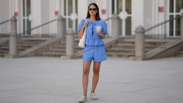 MUNICH, GERMANY - JUNE 15: Anna Winter is seen wearing a blue white striped shorts with drawstring detail from Rita Montezuma x NA-KD; a matching blue white striped blouse with tie and bow details in the front and puff sleeves from Rita Montezuma x NA-KD; a pair of off-white suede Boston slippers with rounded shape and open back from Birkenstock; a light cream white small Romy hobo leather bag with a slim shoulder strap and silver button logo detail from Tory Burch; a cream white reusable to go coffee cup with structural details from Huskee; a yellow golden B.zero 1 necklace with characteristic round pendant from Bvlgari; black rectangular Teru sunglasses from Ray-Ban; a golden Juste un Clou ring from Cartier; a golden Love ring from Cartier on June 15, 2025 in Munich, Germany. (Photo by Moritz Scholz/Getty Images)