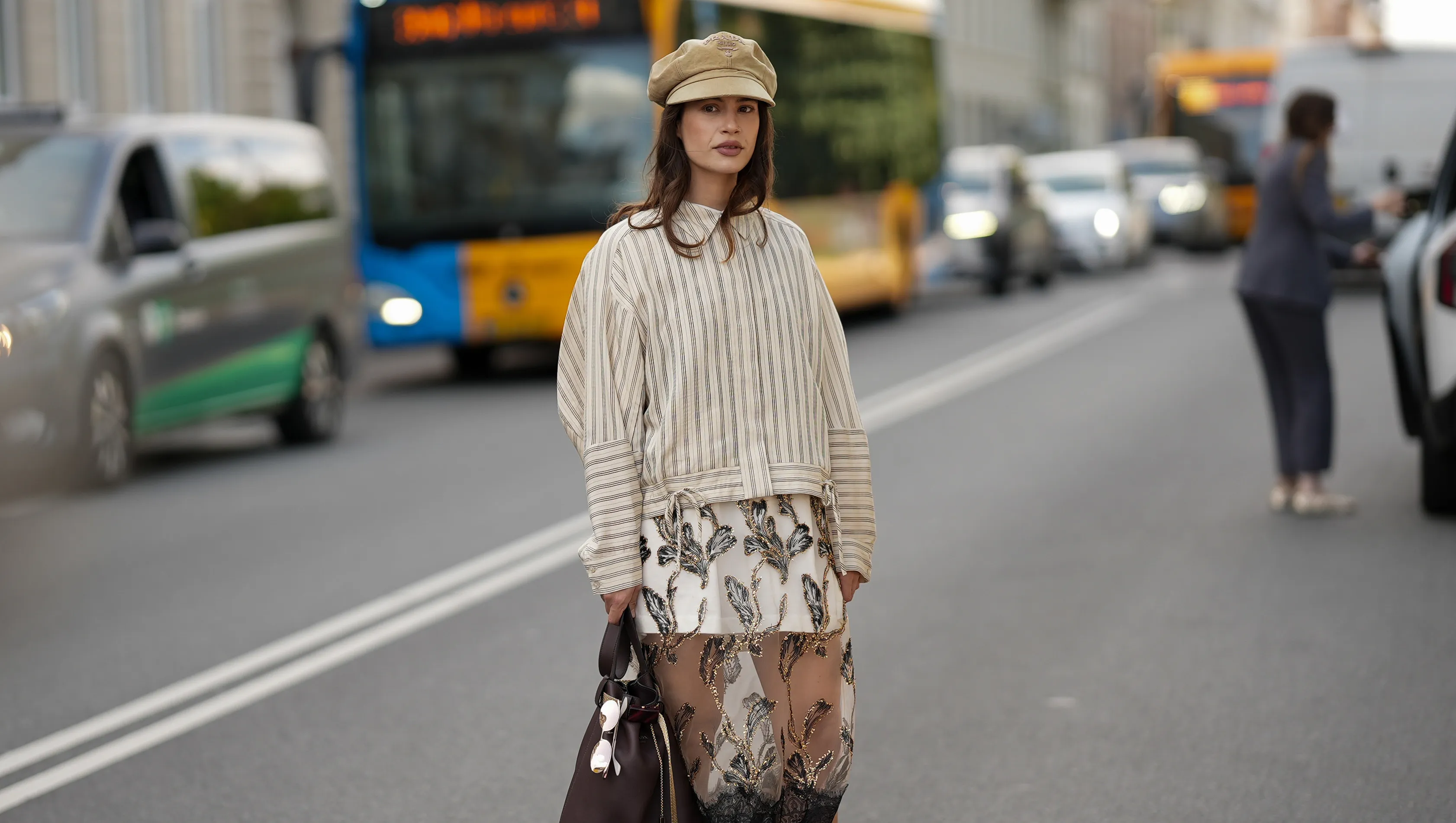 COPENHAGEN, DENMARK - AUGUST 6: Lea Naumann attending the Munthe show during Copenhagen Fashion Week SS26, is seen wearing a Munthe shirt with a vertical stripe pattern in cream color, model is Loasta top, that features a classic pointed collar, drop-shoulder construction and tie details at the bottom; a white mini skirt underneath a black transparent tulle Munthe dress, model Lazo dress, with an all-over gold floral pattern with metallic gold thread and a wide lace trim at the bottom; she carries a brown calfskin Prada Buckle bucket bag with a golden metal mesh belt, long shoulder strap and a printed golden logo on the front; she is wearing a soft Prada baker boy hat in beige cotton with embroidered logo to the front; a pair of Maison Margiela butter tabi flat ballerinas in leather with split toe; her medium-length brunette hair is worn loose with a lightly waved texture during Copenhagen Fashion Week day three on August 6, 2025 in Copenhagen, Denmark. (Photo by Moritz Scholz/Getty Images)