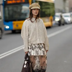 COPENHAGEN, DENMARK - AUGUST 6: Lea Naumann attending the Munthe show during Copenhagen Fashion Week SS26, is seen wearing a Munthe shirt with a vertical stripe pattern in cream color, model is Loasta top, that features a classic pointed collar, drop-shoulder construction and tie details at the bottom; a white mini skirt underneath a black transparent tulle Munthe dress, model Lazo dress, with an all-over gold floral pattern with metallic gold thread and a wide lace trim at the bottom; she carries a brown calfskin Prada Buckle bucket bag with a golden metal mesh belt, long shoulder strap and a printed golden logo on the front; she is wearing a soft Prada baker boy hat in beige cotton with embroidered logo to the front; a pair of Maison Margiela butter tabi flat ballerinas in leather with split toe; her medium-length brunette hair is worn loose with a lightly waved texture during Copenhagen Fashion Week day three on August 6, 2025 in Copenhagen, Denmark. (Photo by Moritz Scholz/Getty Images)