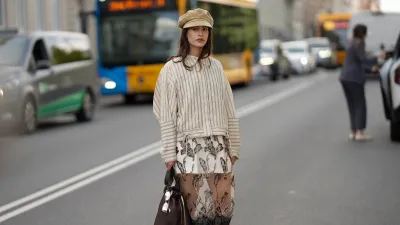 COPENHAGEN, DENMARK - AUGUST 6: Lea Naumann attending the Munthe show during Copenhagen Fashion Week SS26, is seen wearing a Munthe shirt with a vertical stripe pattern in cream color, model is Loasta top, that features a classic pointed collar, drop-shoulder construction and tie details at the bottom; a white mini skirt underneath a black transparent tulle Munthe dress, model Lazo dress, with an all-over gold floral pattern with metallic gold thread and a wide lace trim at the bottom; she carries a brown calfskin Prada Buckle bucket bag with a golden metal mesh belt, long shoulder strap and a printed golden logo on the front; she is wearing a soft Prada baker boy hat in beige cotton with embroidered logo to the front; a pair of Maison Margiela butter tabi flat ballerinas in leather with split toe; her medium-length brunette hair is worn loose with a lightly waved texture during Copenhagen Fashion Week day three on August 6, 2025 in Copenhagen, Denmark. (Photo by Moritz Scholz/Getty Images)