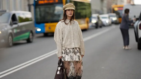 COPENHAGEN, DENMARK - AUGUST 6: Lea Naumann attending the Munthe show during Copenhagen Fashion Week SS26, is seen wearing a Munthe shirt with a vertical stripe pattern in cream color, model is Loasta top, that features a classic pointed collar, drop-shoulder construction and tie details at the bottom; a white mini skirt underneath a black transparent tulle Munthe dress, model Lazo dress, with an all-over gold floral pattern with metallic gold thread and a wide lace trim at the bottom; she carries a brown calfskin Prada Buckle bucket bag with a golden metal mesh belt, long shoulder strap and a printed golden logo on the front; she is wearing a soft Prada baker boy hat in beige cotton with embroidered logo to the front; a pair of Maison Margiela butter tabi flat ballerinas in leather with split toe; her medium-length brunette hair is worn loose with a lightly waved texture during Copenhagen Fashion Week day three on August 6, 2025 in Copenhagen, Denmark. (Photo by Moritz Scholz/Getty Images)