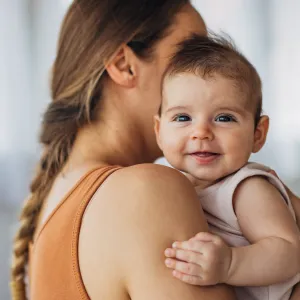 Portrait of a cute smiling baby girl looking directly at the camera while enjoying being in her mother's arms