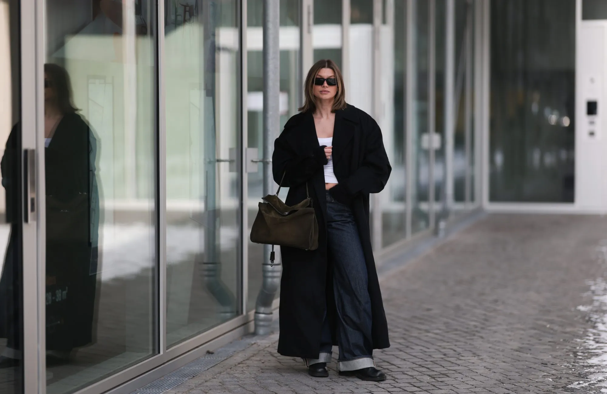 BERLIN, GERMANY - FEBRUARY 19: Sophia Geiss is seen wearing an oversized Bondi black coat layered over a fitted Black Palms top, styled with Acne Studios jeans in a relaxed, straight-leg silhouette. She completes the look with Alohas shoes, adding a clean and modern finish. Accessories include oversized Prada shades with bold frames and a Balenciaga Rodeo suede bag on February 19, 2026 in Berlin, Germany. (Photo by Jeremy Moeller/Getty Images)