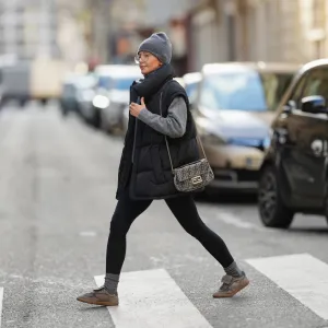 PARIS, FRANCE - JANUARY 15: Diane Batoukina wears long straight brown hair tucked under a ribbed grey cashmere beanie hat by Mango, Kaleos rectangular eyeglasses with thin dark frames, a matching grey cashmere scarf by Mango wrapped around the neck, a medium grey knit sweater by Zara with a high neckline, a black quilted padded sleeveless puffer jacket by WRSTBHVR featuring a matte finish and snap-button front, black stretch leggings by Zara with a smooth matte texture, ribbed grey cashmere socks by Mango worn above the ankle, grey and taupe lace-up sneakers by Alohas with a low-profile rubber sole, and a small grey Fendi monogram shoulder bag with a flap closure and metal chain strap carried at the side, during a street style fashion photo session, on January 15, 2026 in Paris, France. (Photo by Edward Berthelot/Getty Images)