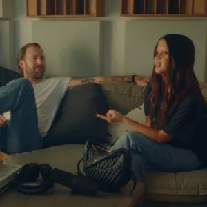Charles Kelley and Maren Morris sitting on a couch in their "Can't Be Alone Tonight" visualizer.