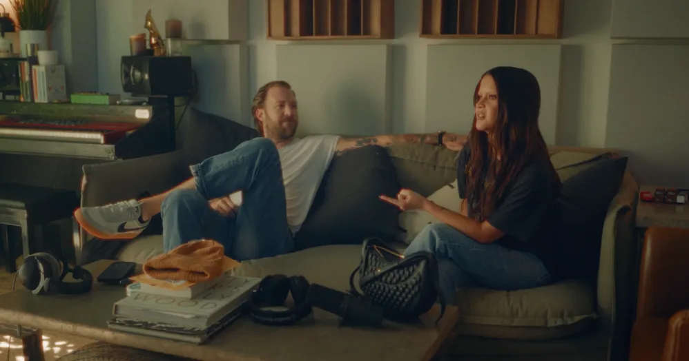 Charles Kelley and Maren Morris sitting on a couch in their "Can't Be Alone Tonight" visualizer.