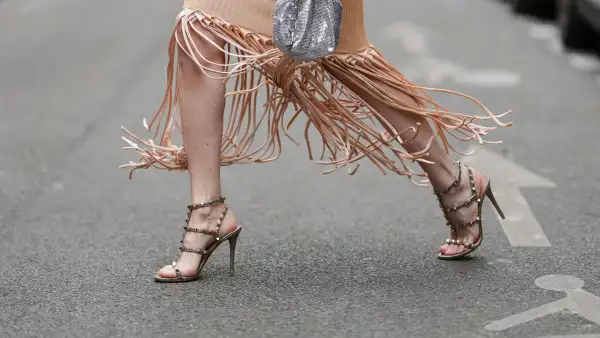 PARIS, FRANCE - MAY 06: Emy Venturini wears a vibrant red leather jacket with button details at the cuffs. The dress from Bottega Veneta is a beige ribbed knit with long, flowing fringe detailing at the hem. A small, silver sequin bag from Rabanne is held in hand. Footwear consists of strappy high-heeled sandals in a neutral tone, embellished with metallic studs from Valentino, during a street style fashion photo session, on May 06, 2025 in Paris, France. (Photo by Edward Berthelot/Getty Images)