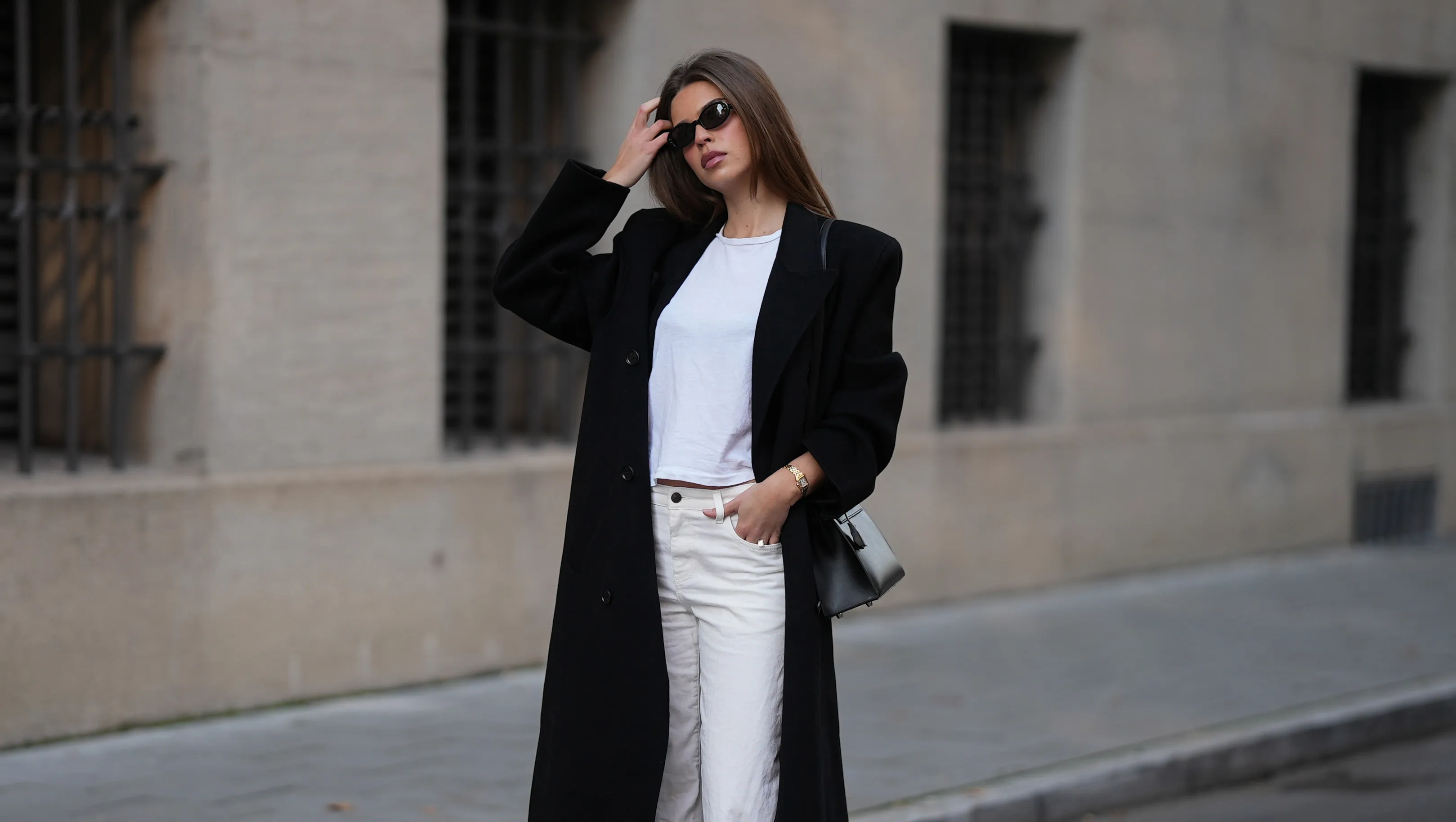MUNICH, GERMANY - NOVEMBER 5: Iva Nikolina is seen wearing a long black wool coat with structured shoulders and a straight silhouette by Almada Label; a white fitted cotton crewneck T-shirt by Re/Done; white wide-leg jeans in a straight leg cut by The Row; black polished leather loafers with a gold logo detail by Saint Laurent; a structured black leather ‚ÄúKelly‚Äù handbag with silver hardware by Herm√®s; a small gold ‚ÄûPanth√©re‚Äú watch by Cartier; narrow oval black sunglasses by Selima Optique; her brown hair is worn straight and parted in the middle on November 5, 2025 in Munich, Germany. (Photo by Moritz Scholz/Getty Images)