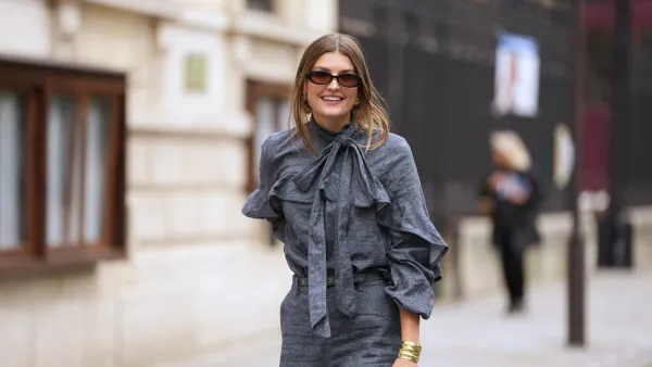 PARIS, FRANCE - OCTOBER 06: A guest wears black square sunglasses, a gray blue denim ruffled high neck / knot bow tie / long sleeves blouse, matching gray blue flared suit pants, outside Zimmermann, during Paris Fashion Week - Womenswear Spring Summer 2026, on October 06, 2025 in Paris, France (Photo by Edward Berthelot/Getty Images)