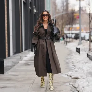 NEW YORK, NEW YORK - FEBRUARY 11: Tamara Kalinic wears oversized black sunglasses, a diamond necklace, a black leather bag, a brown trench coat with a black textured leather collar and a matching belt, a black midi dress, black leather gloves, pale pastel yellow leopard print boots, outside Proenza Schouler, during New York Fashion Week, on February 11, 2026 in New York City (Photo by Edward Berthelot/Getty Images)