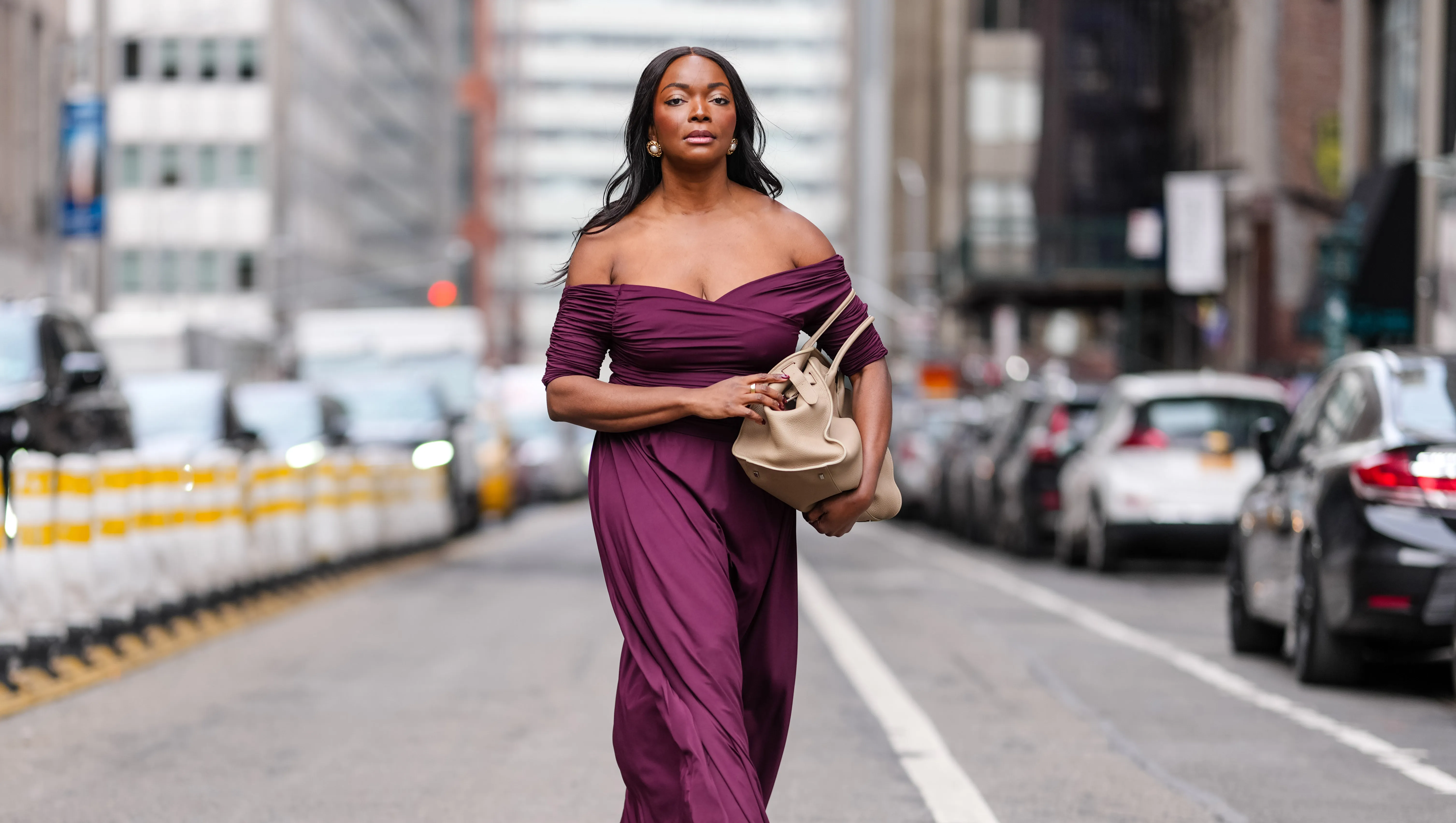 NEW YORK, NEW YORK - FEBRUARY 08: Coco Bassey wears silver earrings, burgundy bordeaux off the shoulder short sleeve Altuzarra maxi dress, shiny light brown leather bag, outside Altuzarra, during the New York Fashion week Fall/Winter 2025 on February 8, 2025 in New York, New York. (Photo by Edward Berthelot/Getty Images)