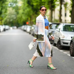 PARIS, FRANCE - AUGUST 02: Gabriella Berdugo wears Loewe sunglasses, a golden large maxi chain necklace, a blue top, a long shirt with colored printed landscape details from Icicle, a matching pleated midi skirt with printed landscape details from Icicle, a white Prada bag, a leather brown large belt from Barbara Bui, green square sandals from Reike Nen, on August 02, 2021 in Paris, France. (Photo by Edward Berthelot/Getty Images)