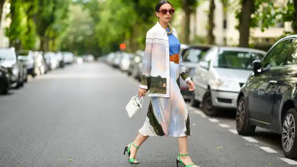 PARIS, FRANCE - AUGUST 02: Gabriella Berdugo wears Loewe sunglasses, a golden large maxi chain necklace, a blue top, a long shirt with colored printed landscape details from Icicle, a matching pleated midi skirt with printed landscape details from Icicle, a white Prada bag, a leather brown large belt from Barbara Bui, green square sandals from Reike Nen, on August 02, 2021 in Paris, France. (Photo by Edward Berthelot/Getty Images)