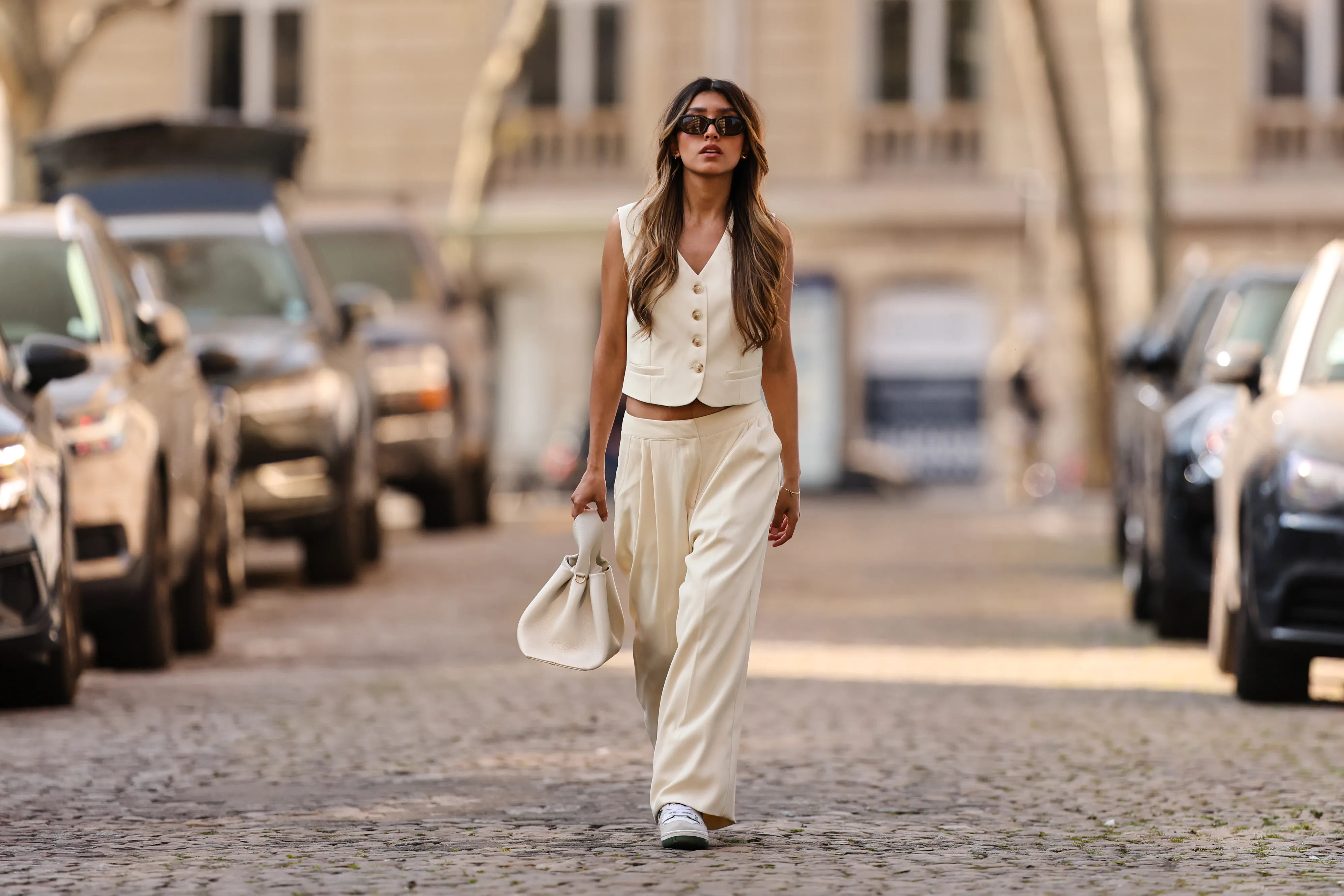 PARIS, FRANCE - MARCH 26: Angela Gonzalez wears black sunglasses, silver earrings, a white latte buttoned / sleeveless / linen gilet, matching white latte palazzo pants, a white matte leather handbag, white and dark green details leather sneakers from New Balance, during a street style fashion photo session, on March 26, 2022 in Paris, France. (Photo by Edward Berthelot/Getty Images)