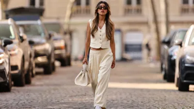 PARIS, FRANCE - MARCH 26: Angela Gonzalez wears black sunglasses, silver earrings, a white latte buttoned / sleeveless / linen gilet, matching white latte palazzo pants, a white matte leather handbag, white and dark green details leather sneakers from New Balance, during a street style fashion photo session, on March 26, 2022 in Paris, France. (Photo by Edward Berthelot/Getty Images)