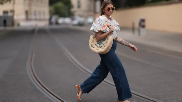 Aline Kaplan wearing Baum & Pferdgarten wide leg blue denim pants, & other stories white flower pattern cropped blouse and orange summer heels and Mango orange black shades on June 06, 2023 in Berlin, Germany.