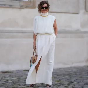 COPENHAGEN, DENMARK - AUGUST 7: Renia Jaz wears black sunglasses, gold necklace, white high neck fringe sleeveless shirt, white maxi skirt with high slit, light brown bag, light blue Fendi lollipop leather holder, dark brown mule heels, outside The Garment, during the Copenhagen Fashion Week Spring/Summer 2024-2025 on August 7, 2024 in Copenhagen, Denmark. (Photo by Edward Berthelot/Getty Images)