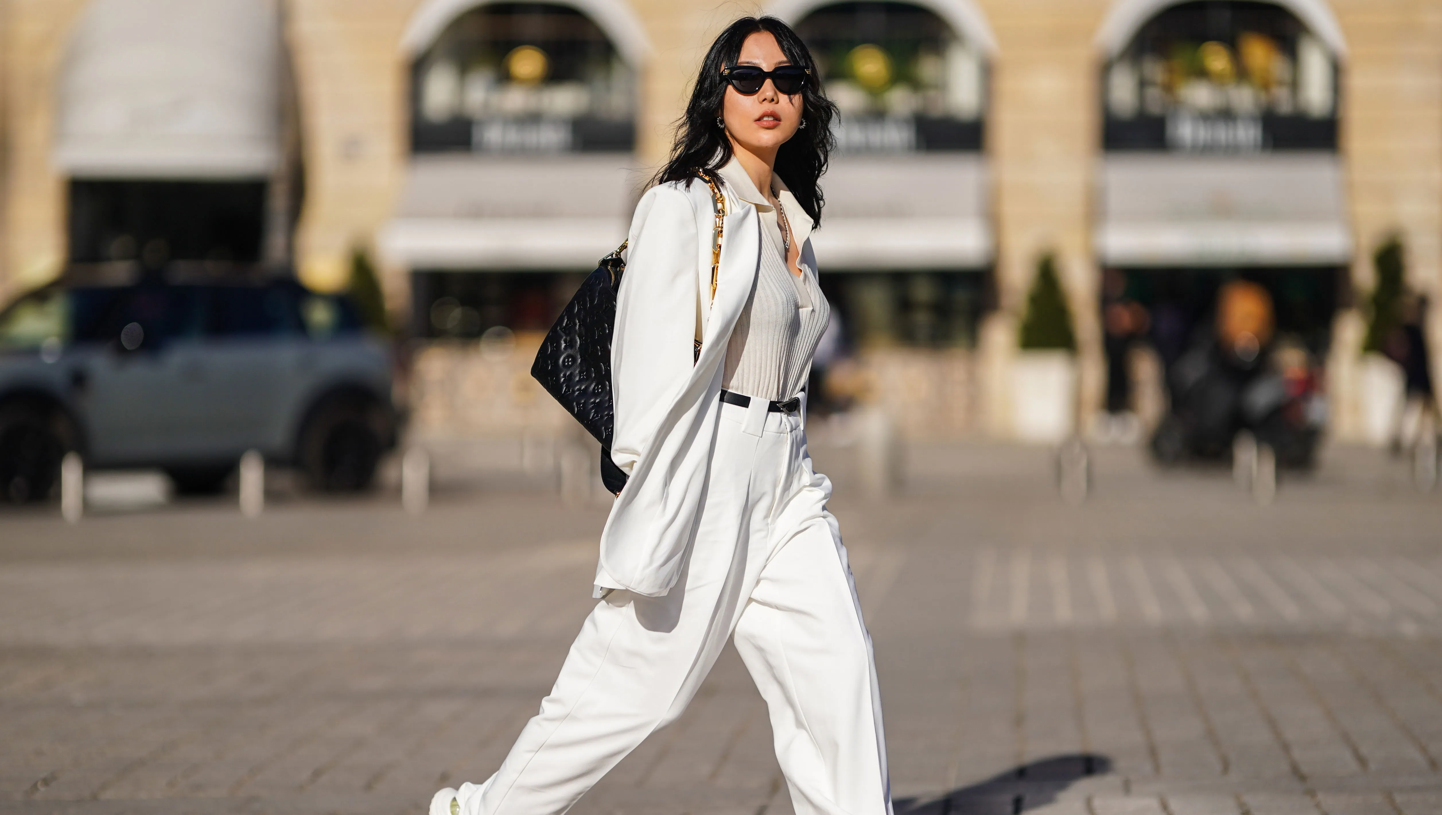PARIS, FRANCE - FEBRUARY 27: Xiayan wears black Bottega Veneta sunglasses, silver earrings, a silver chain necklace, a white V-neck silk gown, a white long oversized Sundarbay blazer jacket with white suit Sundarbay matching pants, a black shiny leather belt, white and beige with gold details Stellaluna sneakers, a black shiny leather Louis Vuitton monogram-embossed Coussin PM crossbody bag, on February 27, 2021 in Paris, France. (Photo by Edward Berthelot/Getty Images)