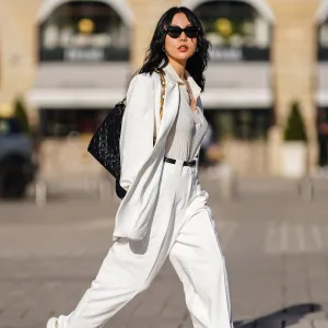 PARIS, FRANCE - FEBRUARY 27: Xiayan wears black Bottega Veneta sunglasses, silver earrings, a silver chain necklace, a white V-neck silk gown, a white long oversized Sundarbay blazer jacket with white suit Sundarbay matching pants, a black shiny leather belt, white and beige with gold details Stellaluna sneakers, a black shiny leather Louis Vuitton monogram-embossed Coussin PM crossbody bag, on February 27, 2021 in Paris, France. (Photo by Edward Berthelot/Getty Images)