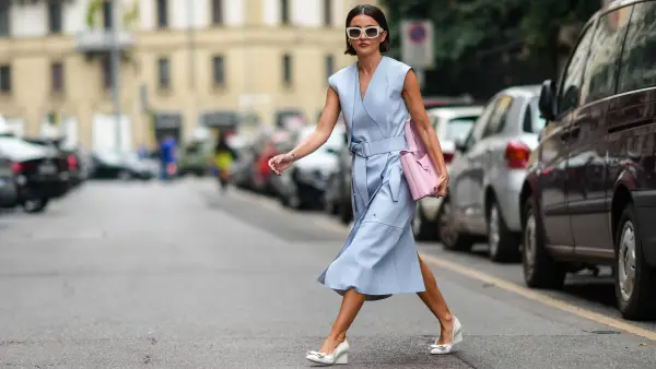 MILAN, ITALY - SEPTEMBER 25: Alexandra Pereira wears white sunglasses, silver and rhinestones earrings, a pale blue shiny leather V-neck / sleeveless / belted / slit midi dress, a pale pink handbag from Salvatore Ferragamo, white leather block heels shoes with embroidered knot on the toe-cap, rings, outside the Ferragamo fashion show during the Milan Fashion Week - Spring / Summer 2022 on September 25, 2021 in Milan, Italy. (Photo by Edward Berthelot/Getty Images)
