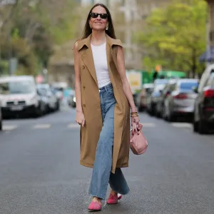 PARIS, FRANCE - APRIL 07: Alba Garavito Torre wears black sunglasses from Ray Ban, gold large earrings, a white tank-top, a beige sleeveless / buttoned long gilet, blue denim ripped wide legs pants, a gold Love bracelet from Cartier, gold bracelets, a pale pink matte leather handbag, pink suede and leather print pattern flat mules from Mimush Madrid, during a street style fashion photo session, on April 07, 2023 in Paris, France. (Photo by Edward Berthelot/Getty Images)