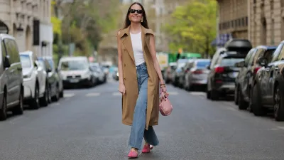 PARIS, FRANCE - APRIL 07: Alba Garavito Torre wears black sunglasses from Ray Ban, gold large earrings, a white tank-top, a beige sleeveless / buttoned long gilet, blue denim ripped wide legs pants, a gold Love bracelet from Cartier, gold bracelets, a pale pink matte leather handbag, pink suede and leather print pattern flat mules from Mimush Madrid, during a street style fashion photo session, on April 07, 2023 in Paris, France. (Photo by Edward Berthelot/Getty Images)