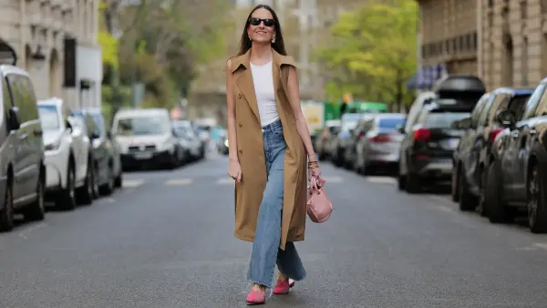 PARIS, FRANCE - APRIL 07: Alba Garavito Torre wears black sunglasses from Ray Ban, gold large earrings, a white tank-top, a beige sleeveless / buttoned long gilet, blue denim ripped wide legs pants, a gold Love bracelet from Cartier, gold bracelets, a pale pink matte leather handbag, pink suede and leather print pattern flat mules from Mimush Madrid, during a street style fashion photo session, on April 07, 2023 in Paris, France. (Photo by Edward Berthelot/Getty Images)