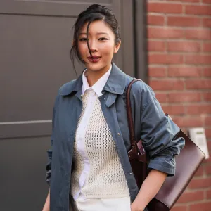 MILAN, ITALY - FEBRUARY 25: A guest wears black hair in a bun, a blue slate cotton trench coat, a white ivory cotton button down mesh / fishnet cardigan shirt, white ivory wide leg suit trousers, a brown burgundy leather shoulder bag, outside Fendi, during Milan Fashion Week - Womenswear Fall/Winter 2026/2027, on February 25, 2026 in Milan, Italy (Photo by Edward Berthelot/Getty Images)